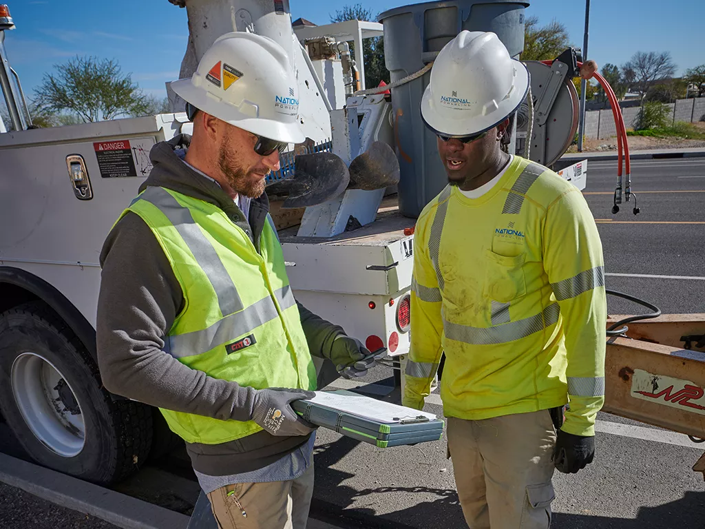 Two National Powerline employees looking at a clipboard on a job site.