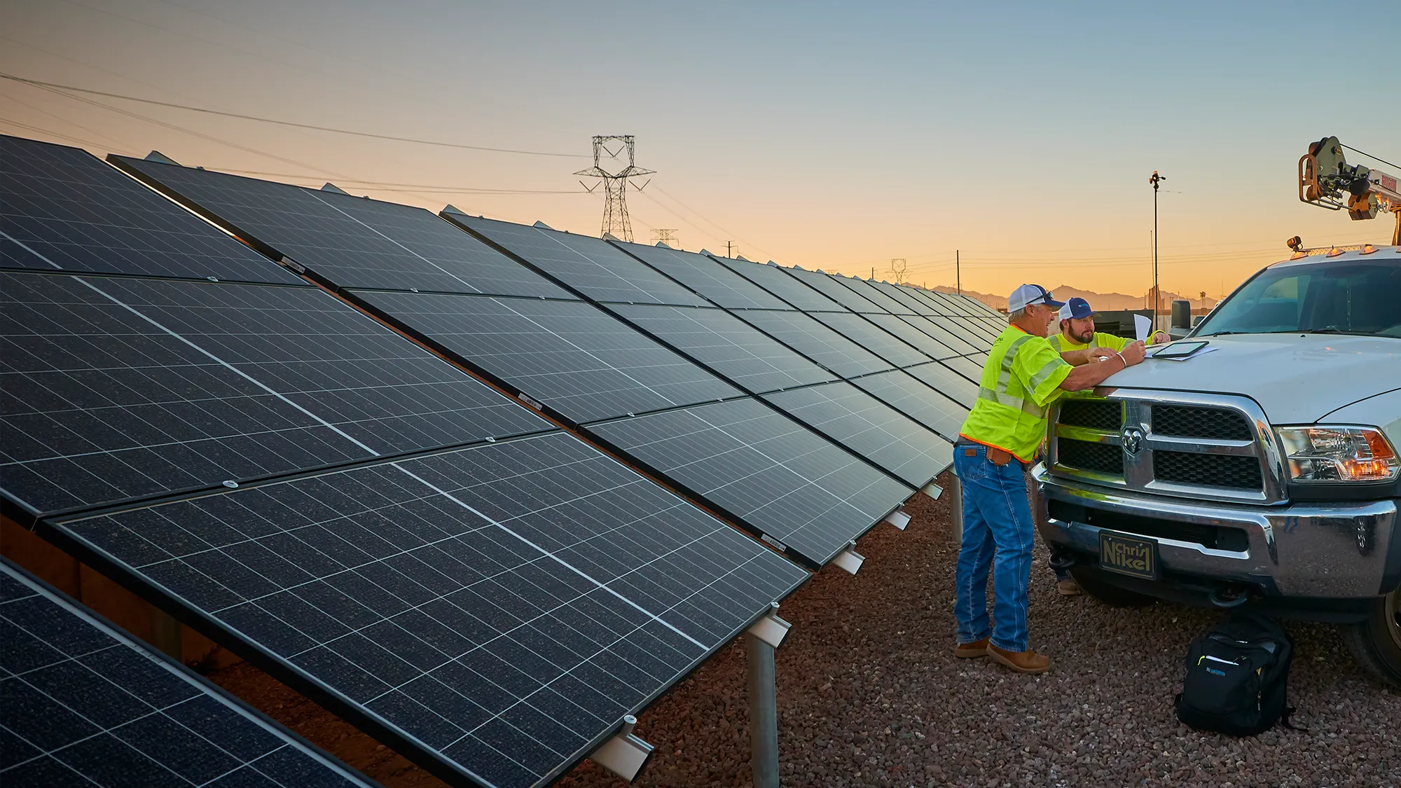 Two National Powerline employees standing in front of a row of solar panels.