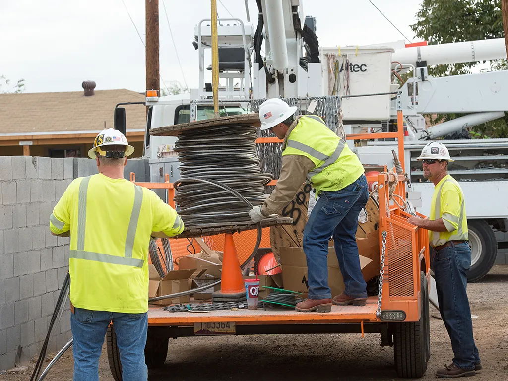 Thee National Powerline workers unloading cable from a trailer.