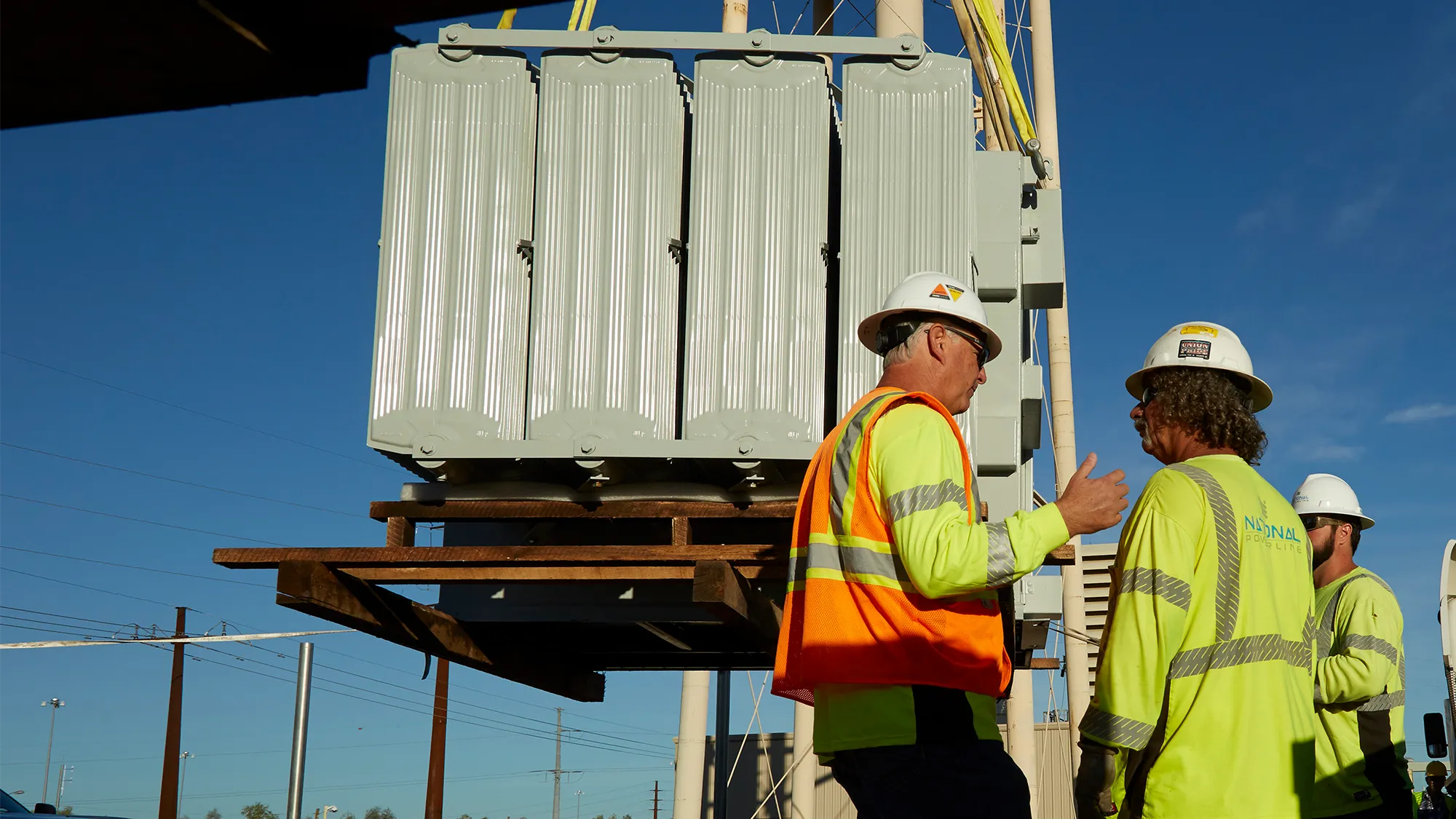 National Powerline supervisor talking to a worker while a substation is hoisted in the background.